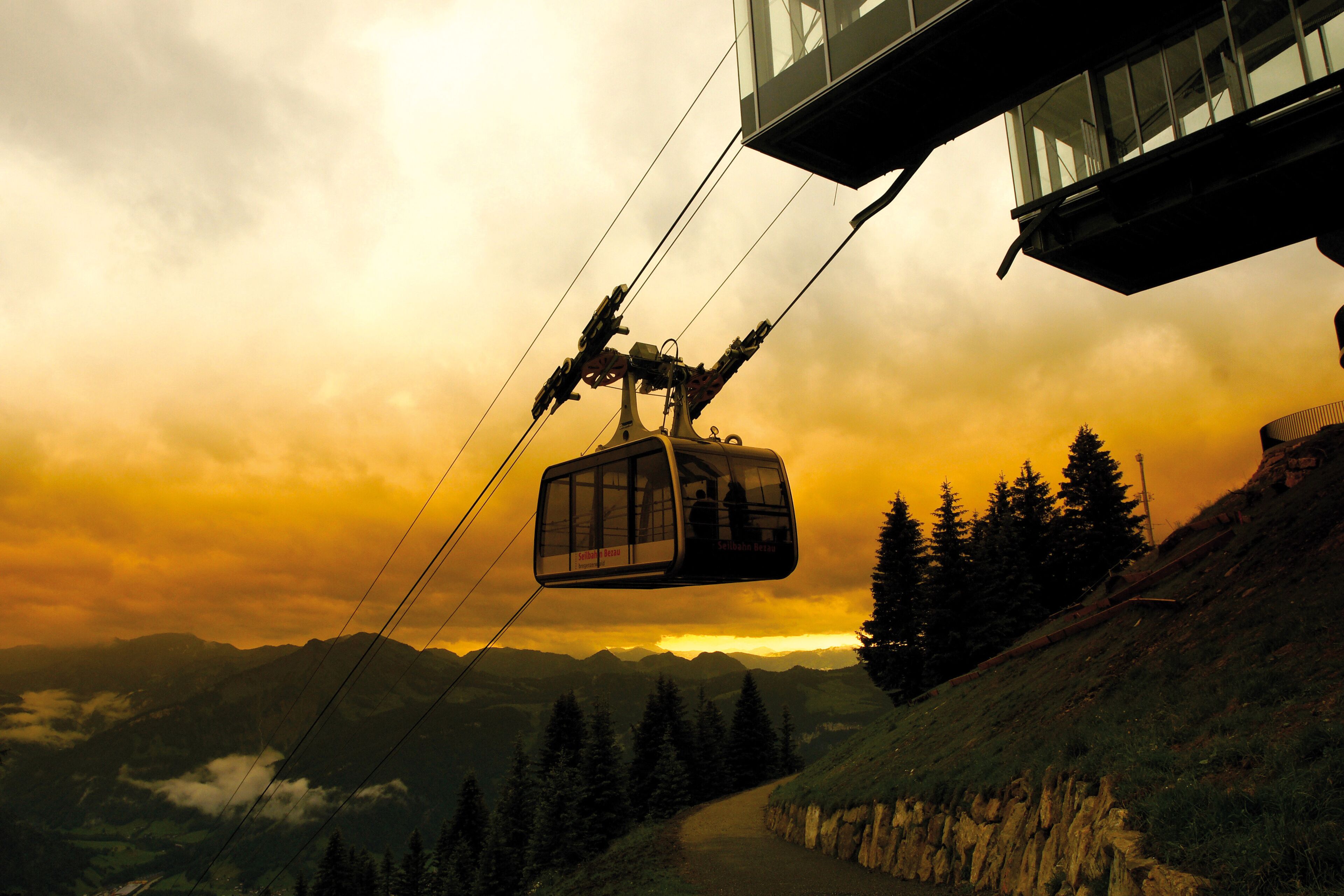 A cable car moving along a mountain path with a sunset in the background.