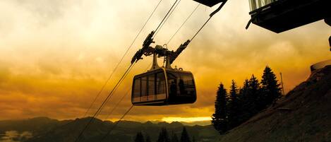 A cable car moving along a mountain path with a sunset in the background.
