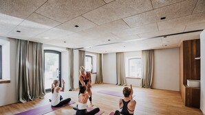Una lezione di yoga in una stanza ampia con pavimento in legno, ampie finestre e tende.