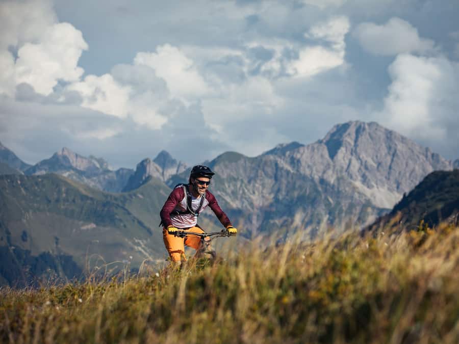 Un ciclista de montaña en un sendero con montañas al fondo.
