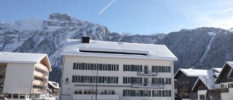 A multi-story building with a snow-covered roof and a ski resort in the background.