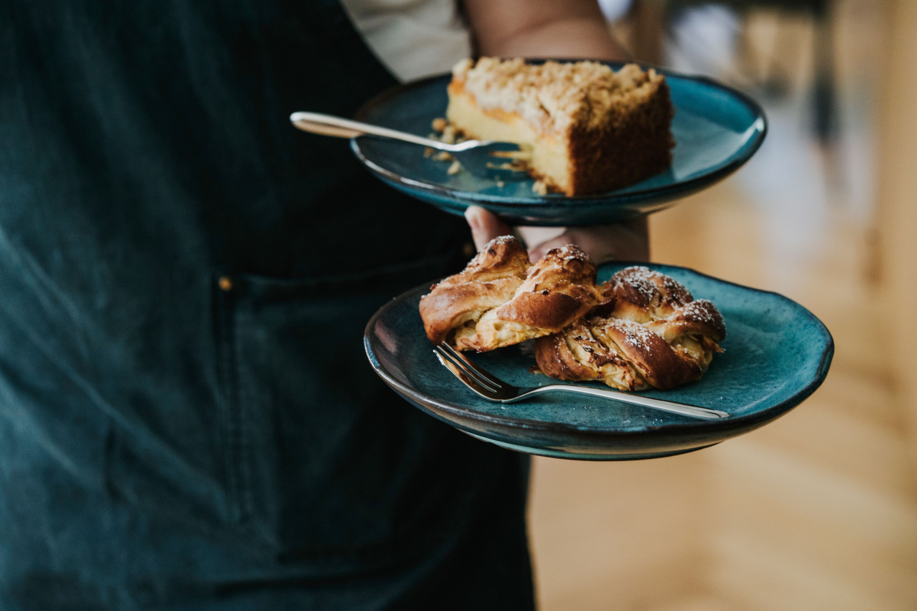 A person holding two plates with food items, one plate has a piece of cake and the other has pastries.