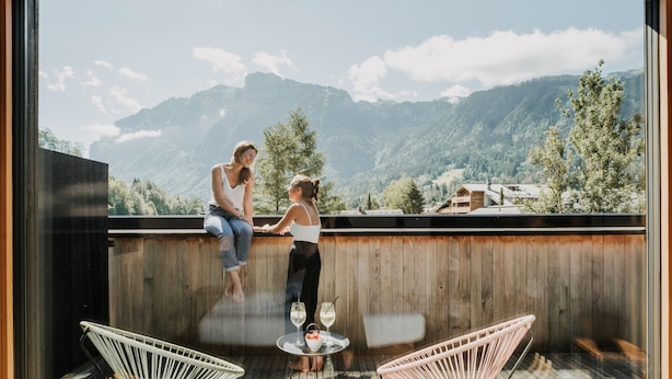Un balcone con due persone sedute, un pavimento in legno e vista sulle montagne.