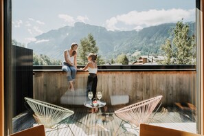 Ein Balkon mit zwei Personen, Holzboden und Blick auf Berge.