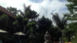 A swimming pool with stone statues, surrounded by lush greenery and a building with a tiled roof.
