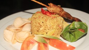 A plate of fried rice with vegetables and a piece of fried chicken on a white plate.