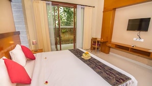 A hotel room with a large bed, a TV mounted on the wall, a small table, and a sliding glass door leading to a balcony.