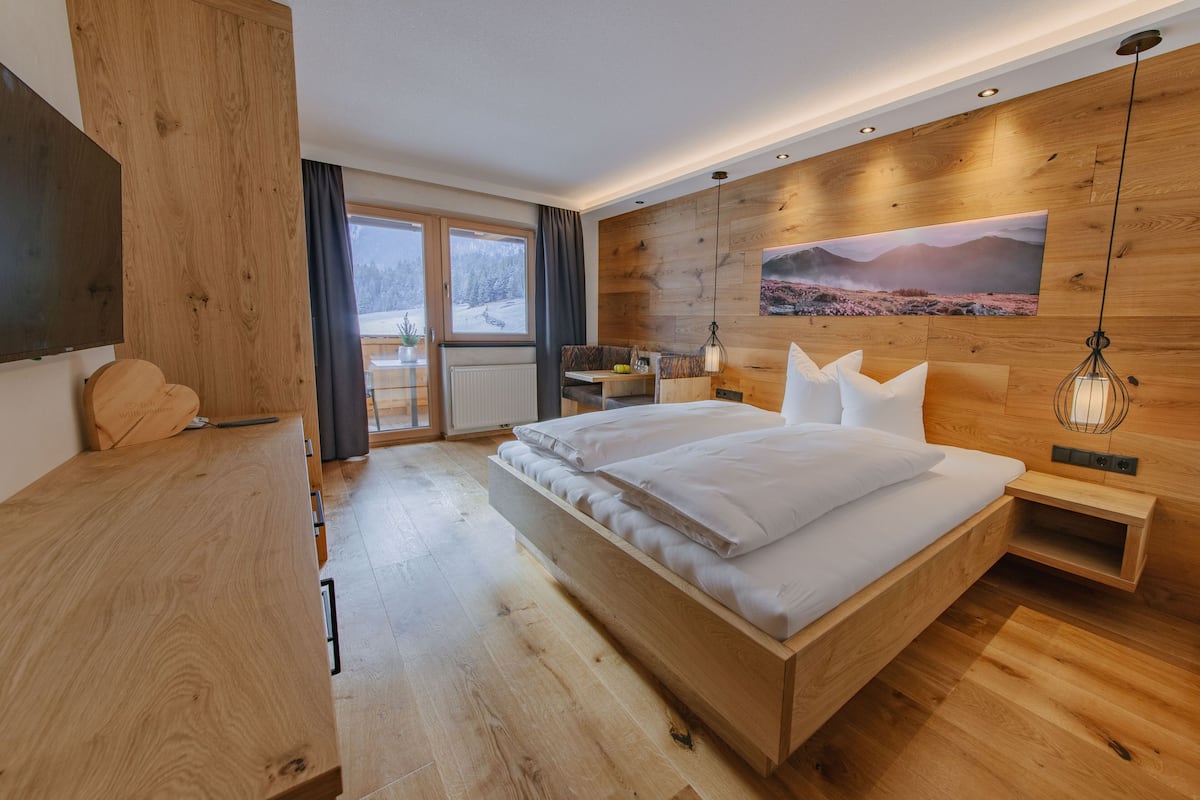 Ein modernes Schlafzimmer mit einem Holzbett, einem Schreibtisch und Blick auf eine verschneite Landschaft durch ein großes Fenster.
