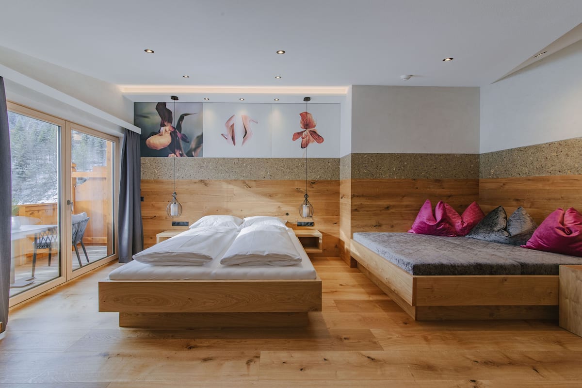 Ein Schlafzimmer mit einem hölzernen Bett, einer Bank mit Kissen und einem großen Fenster.