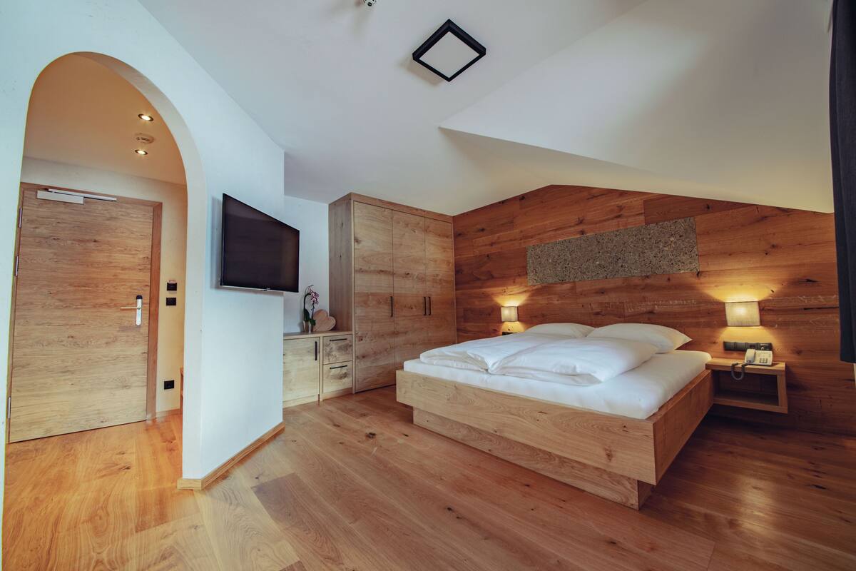 Ein modernes Schlafzimmer mit einem hölzernen Bett, einem an der Wand befestigten Fernseher und einem Holzschrank.