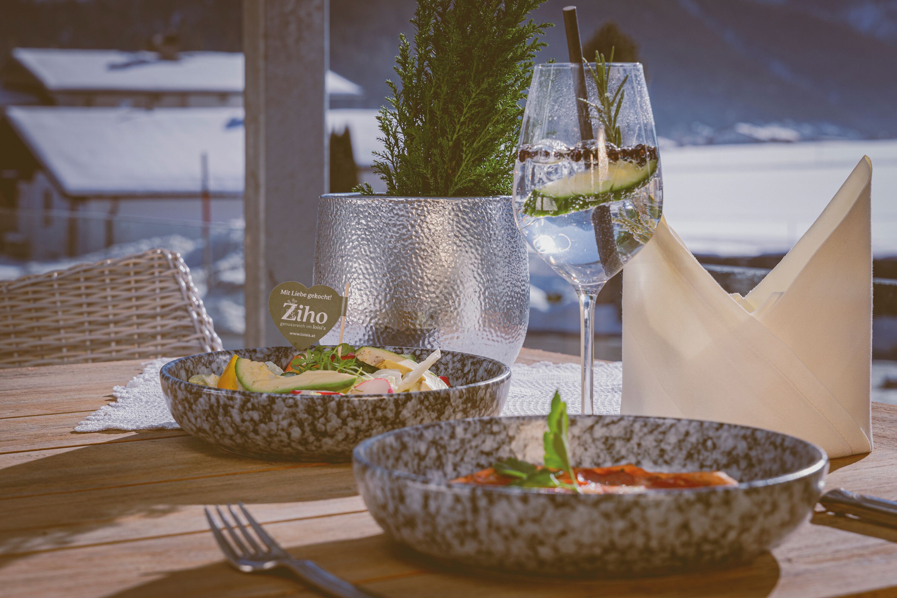 A table set with two bowls of salad, a glass of water with a straw, and a napkin.
