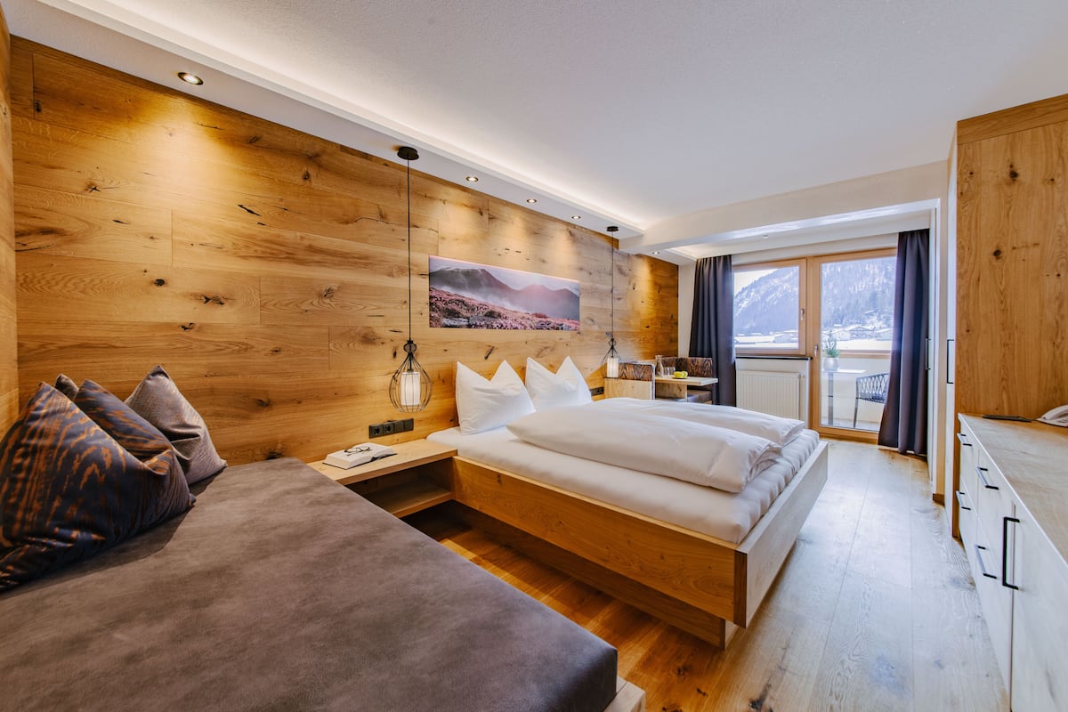 Ein modernes Schlafzimmer mit Holzwand, einem großen Bett, einer Couch und Bergblick aus dem Fenster.