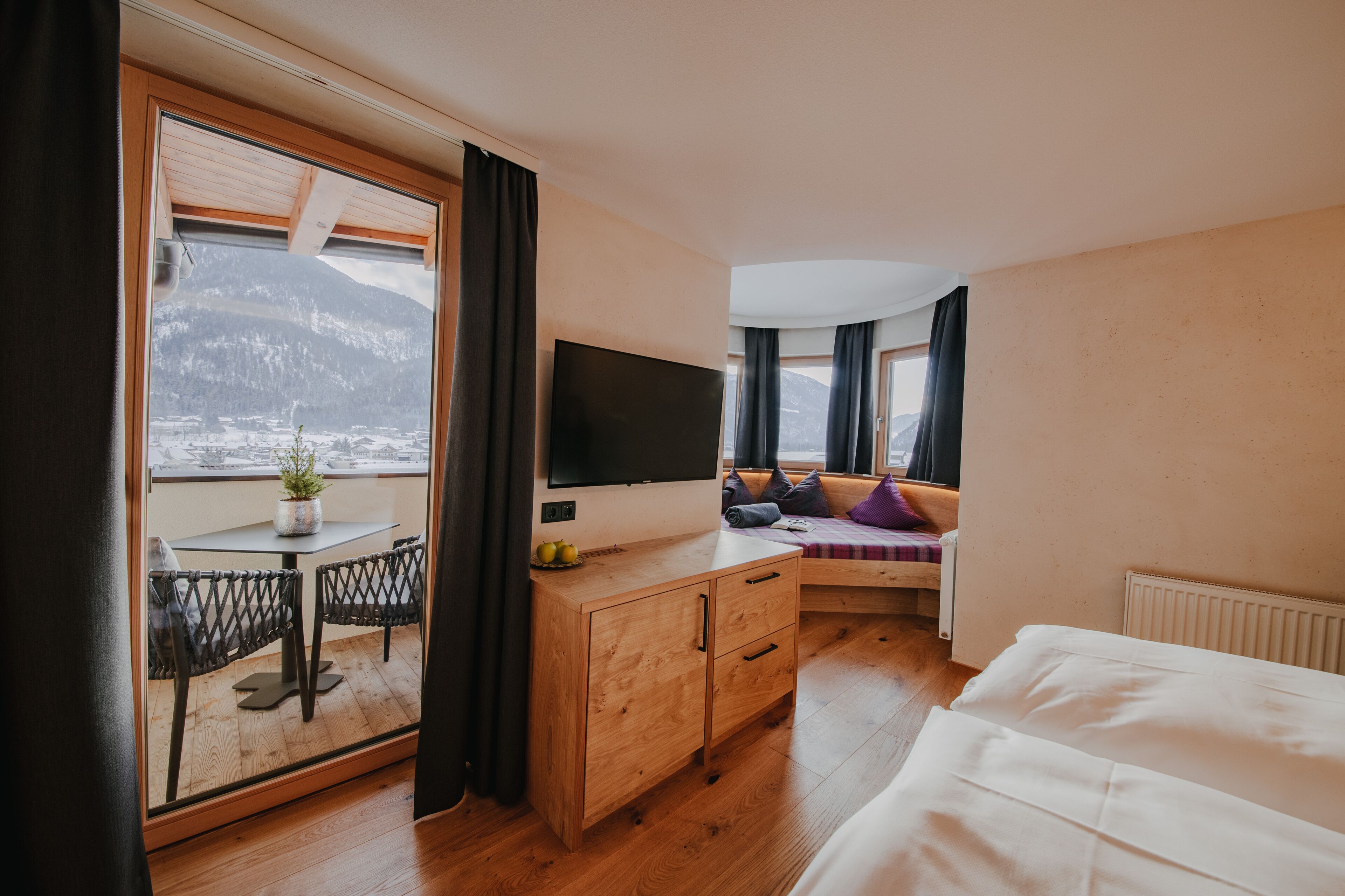 Una habitación de hotel moderna con un ventanal grande, un televisor de pantalla plana, un armario de madera, un sofá y una cama.