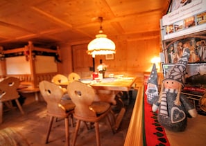 Ein Holzkamin mit einem Esstisch und Stühlen, einer Hängelampe und einem Regal mit einer Puppe und einem Buch.