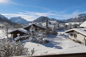 Un village enneigé, avec ses maisons traditionnelles en bois, une piste de ski et des montagnes en arrière-plan.