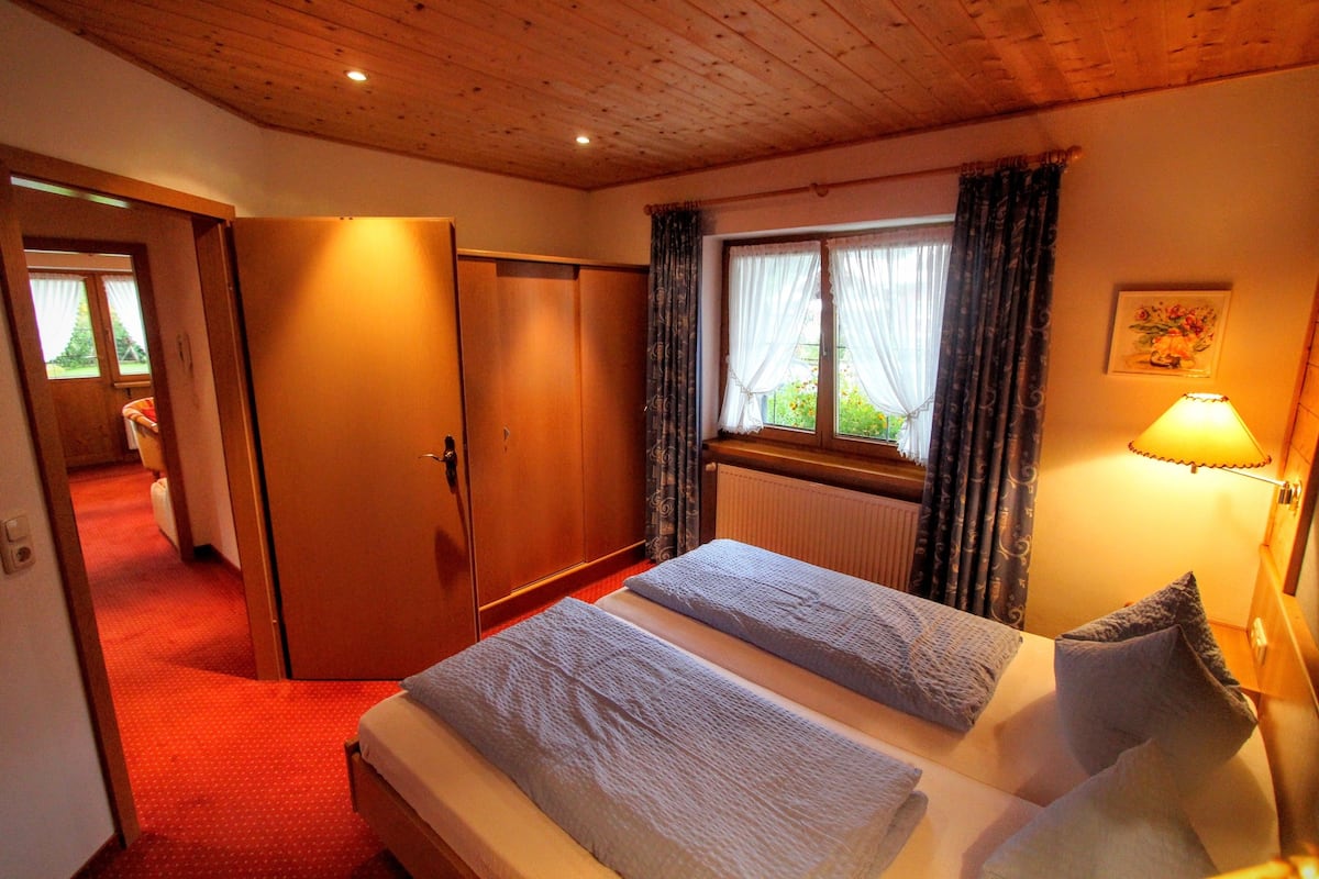 Ein Schlafzimmer mit zwei Betten, Holzboden, einem Fenster mit Vorhängen und einer Lampe.