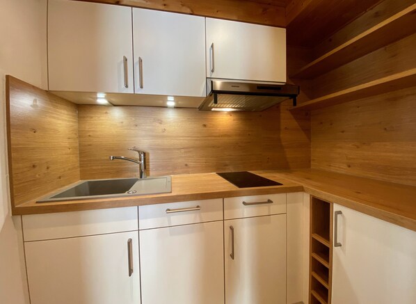 Una cocina compacta con armarios blancos, un lavamanos de acero inoxidable y una estufa empotrada.