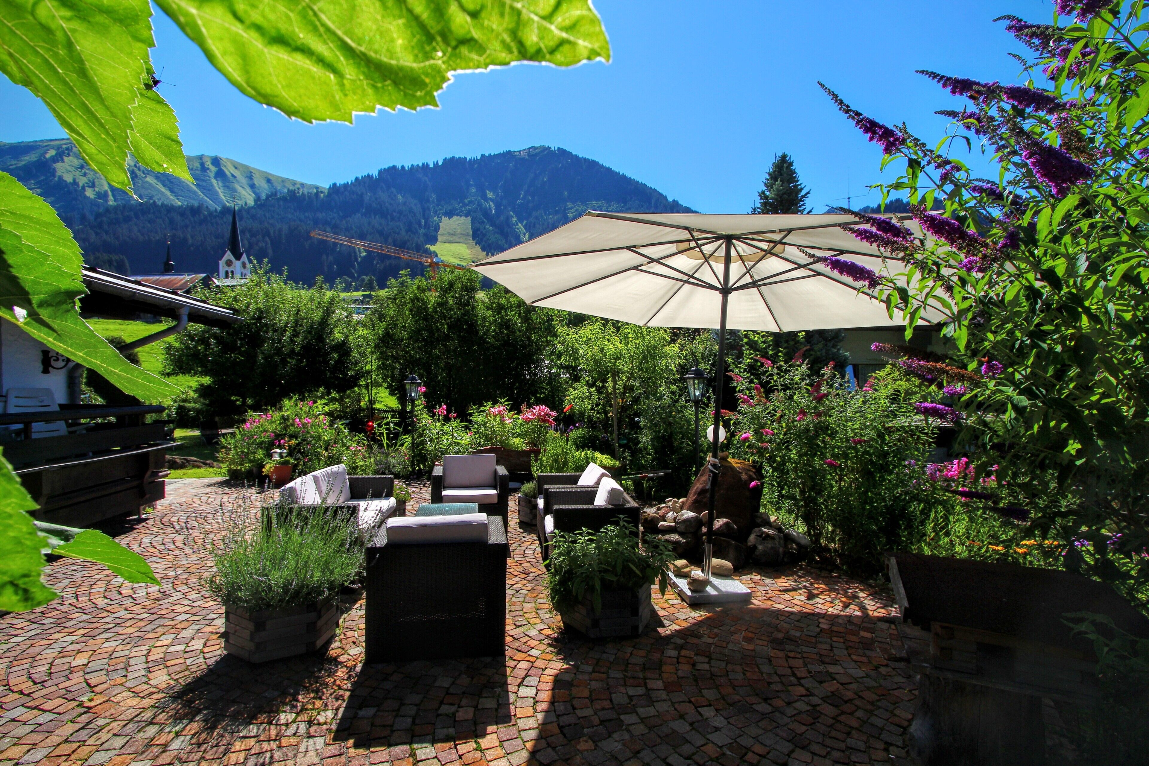 Un patio con mobili da esterno, un ombrellone grande e vista su una montagna e una chiesa sullo sfondo.