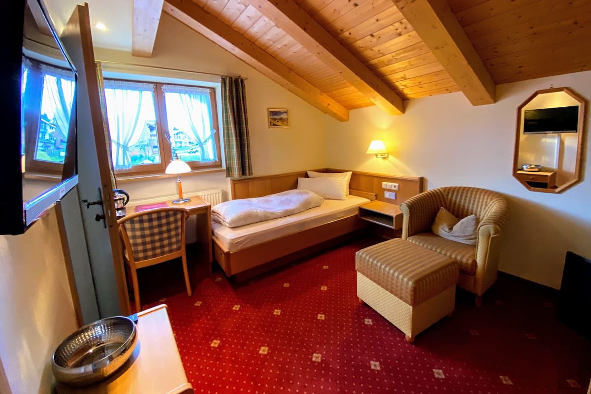 Ein Zimmer mit einem Bett, einem Schreibtisch, einem Stuhl, einem Fernseher und einem Fenster mit Vorhängen.