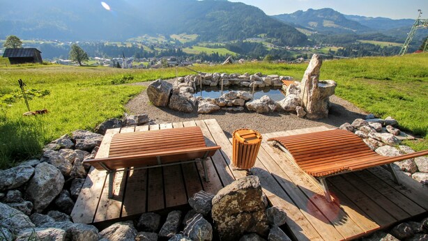Un espace extérieur rustique aménagé avec des bancs en bois et un foyer en pierre, le tout entouré d’un paysage montagneux pittoresque.