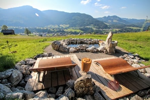 Un espacio al aire libre rústico con bancos de madera y un hogar de piedra, rodeado por un paisaje montañoso pintoresco.