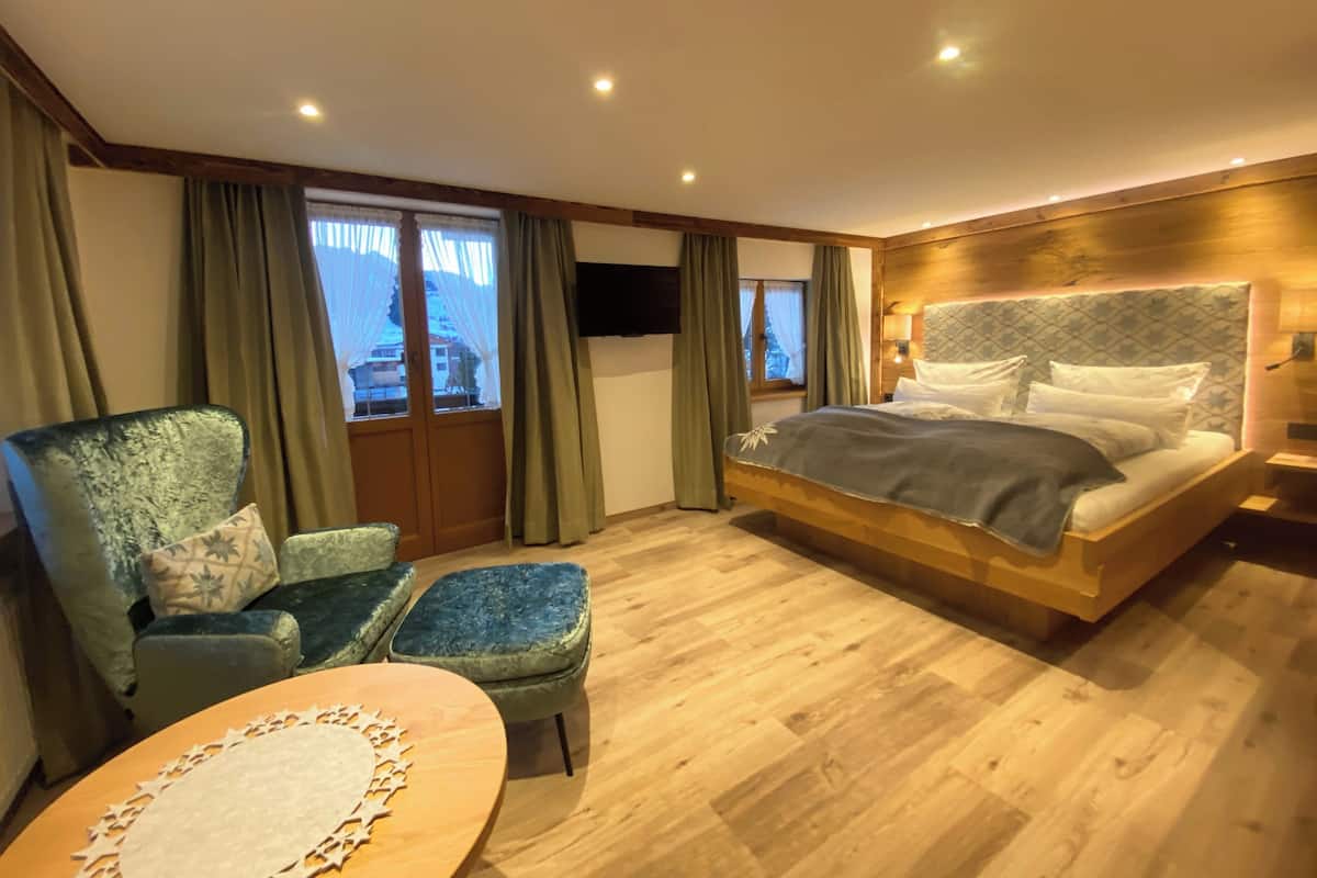 Ein Schlafzimmer mit Bett, Stuhl, kleinem Tisch und einem Fenster mit Vorhängen.