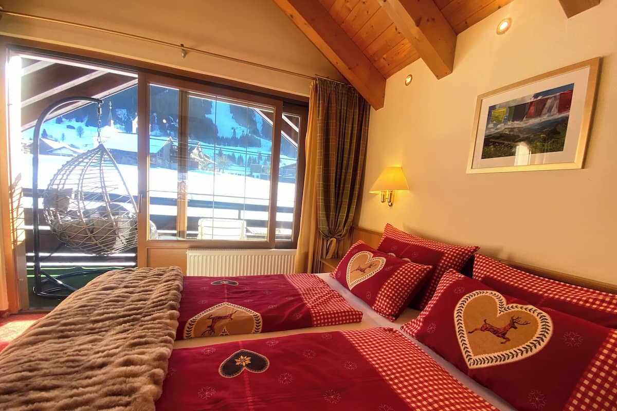 Ein gemütliches Zimmer mit einem großen Fenster, einem Bett mit roter Bettwäsche und einer Holzzieldecke.