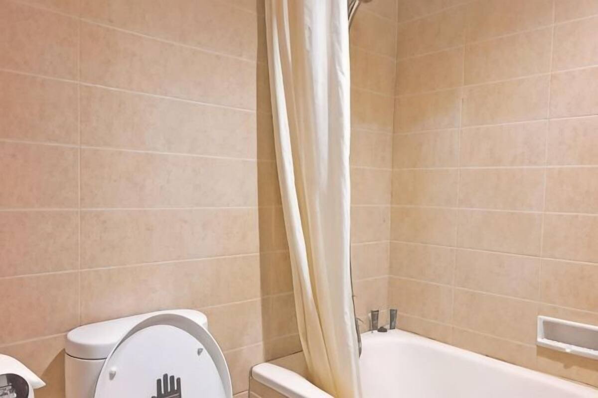 A bathroom with beige tiles, a toilet, a bathtub, and a shower curtain.