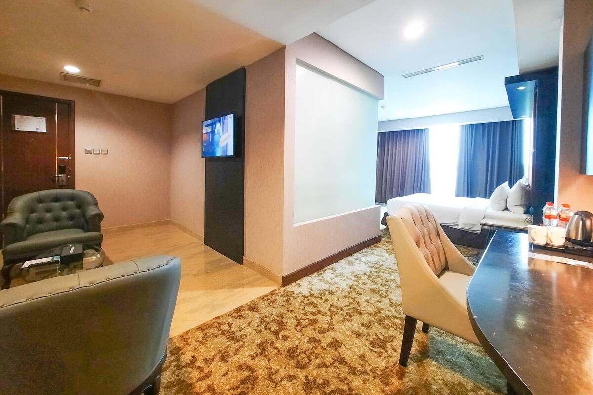 A hotel room with a bed, a desk, a chair, a television, and a carpeted floor.