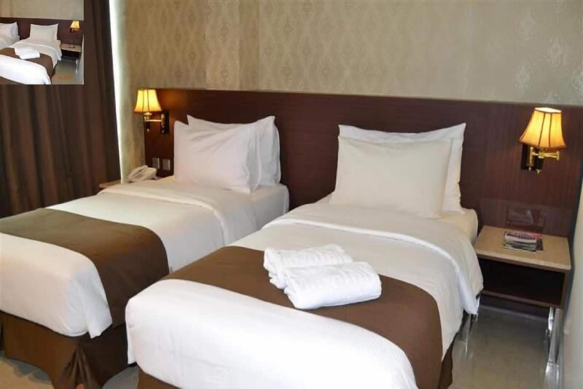 A hotel room with two beds, a nightstand with a lamp, and a wall-mounted phone.