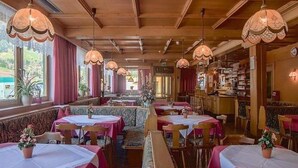 A restaurant with multiple tables and booths, wooden ceiling, and large windows with curtains. - Kolberhof Gasthof (ALPBACH)