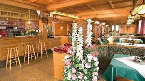A restaurant with wooden ceiling beams, a bar area with stools, and tables set for dining. - Kolberhof Gasthof (ALPBACH)