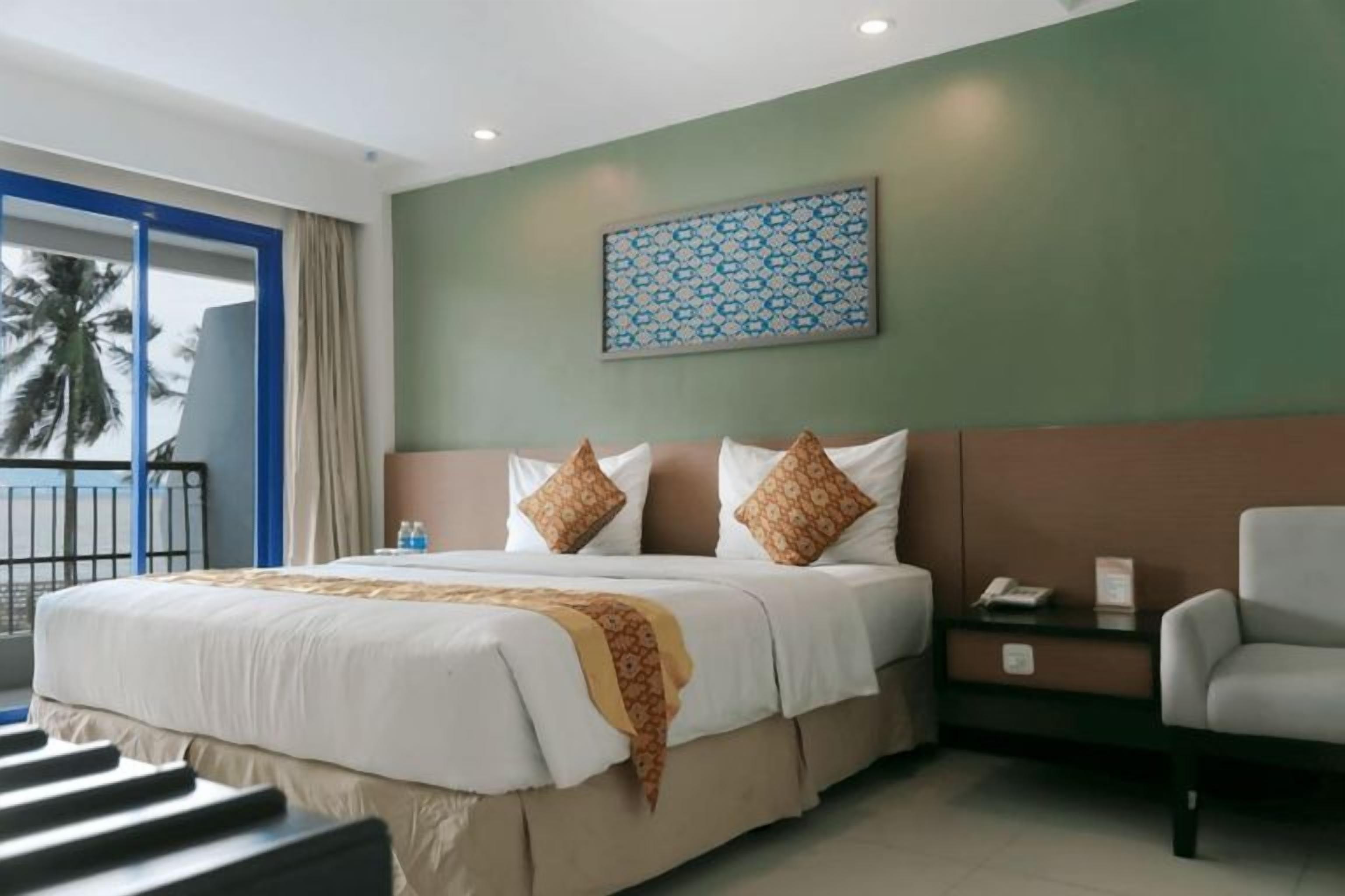 A hotel room with a bed, a chair, a nightstand, and a view of palm trees.
