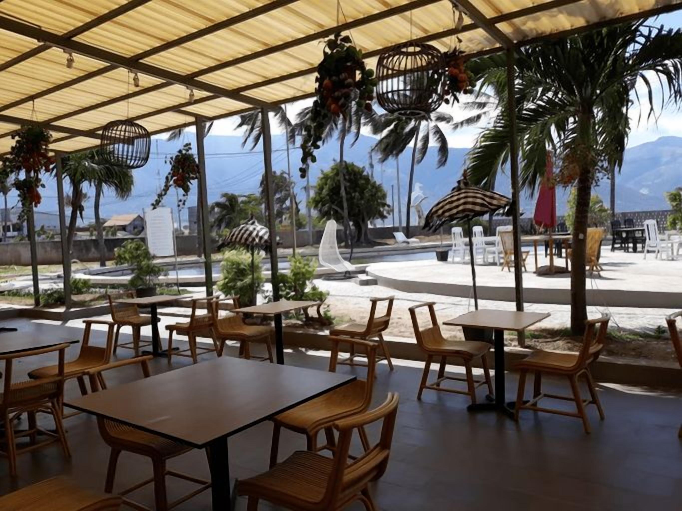 An outdoor seating area with tables and chairs, a covered section with a roof, and a view of the ocean and mountains in the background.