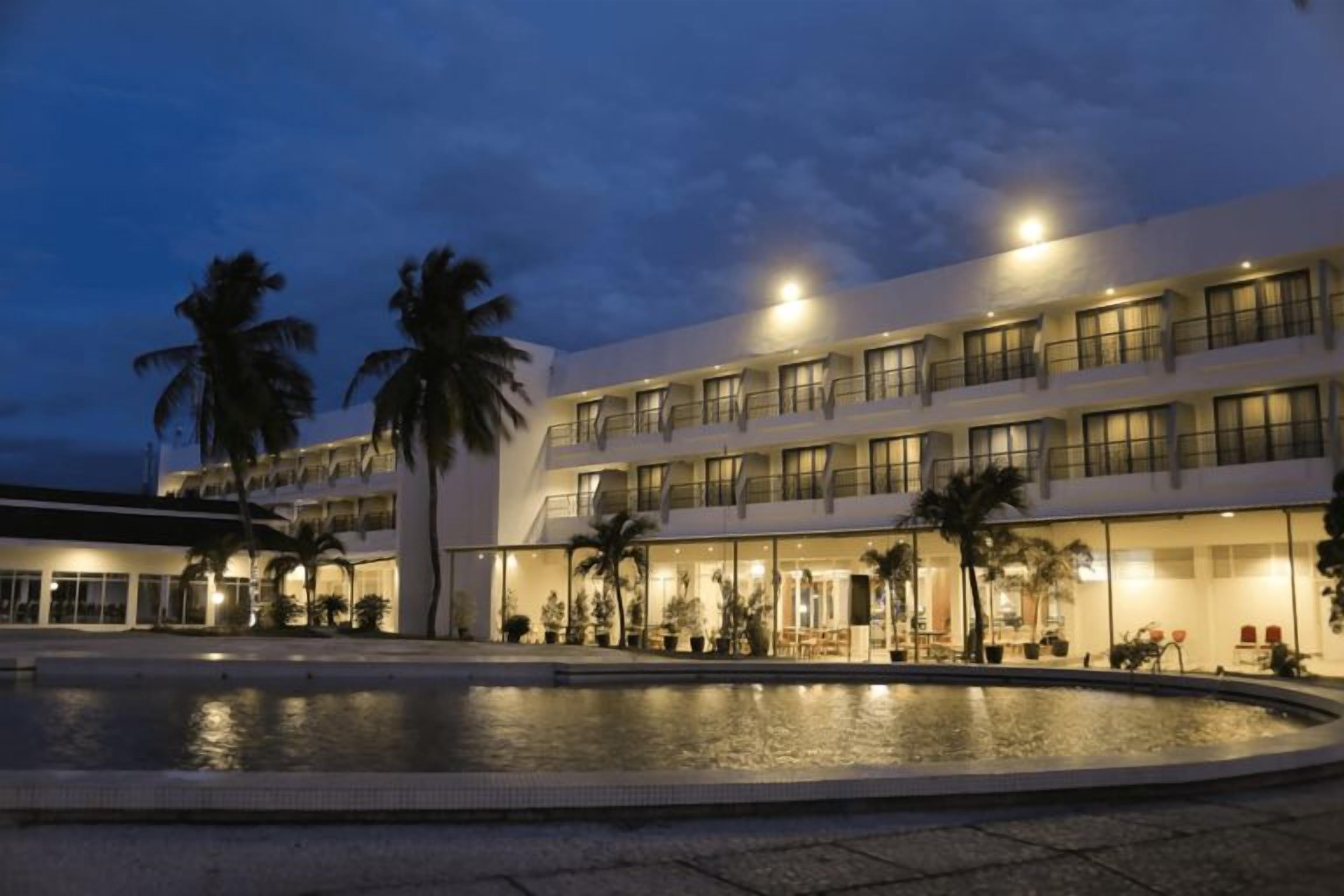 A hotel with a pool, palm trees, and multiple balconies.
