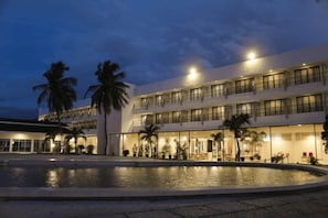 Een hotel met een zwembad, palmbomen en meerdere balkons.