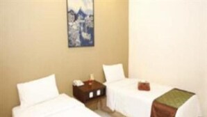 A hotel room with two single beds, a nightstand, and a painting on the wall. - Palu Golden (Palu)