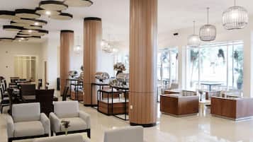 A hotel lobby with seating areas, a reception desk, and large windows.