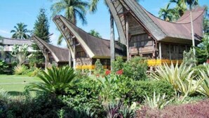 A resort with multiple buildings featuring steeply pitched roofs, surrounded by lush tropical vegetation and palm trees. - Toraja Misiliana (Rinding Batu)