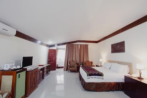 Une chambre d’hôtel avec un lit, une télévision, un bureau avec une lampe, une chaise et une fenêtre avec des rideaux.