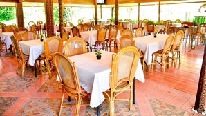 An outdoor dining area with round tables and wicker chairs, covered by a wooden roof, and surrounded by greenery. - Toraja Misiliana (Rinding Batu)