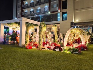 A hotel entrance with a decorative archway, a well-maintained lawn, and a multi-story building in the background.
