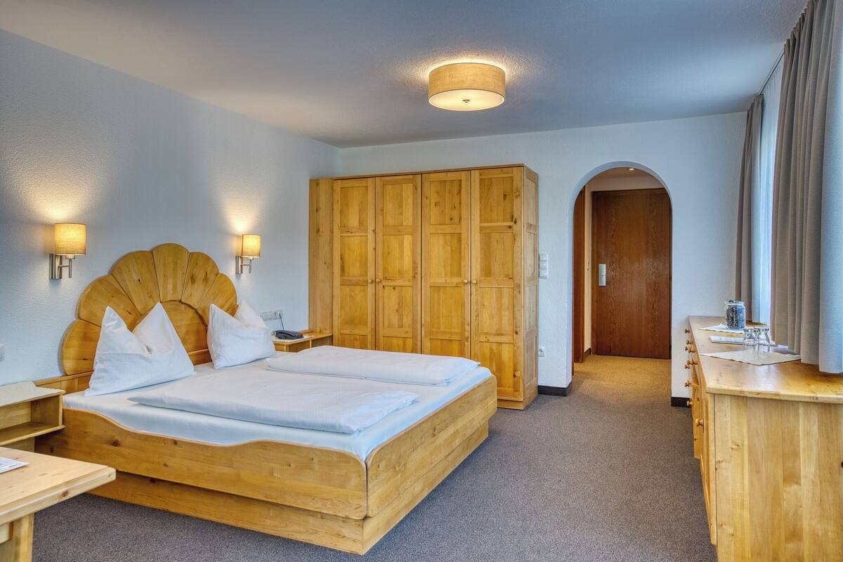 A room with a wooden bed, a wardrobe, a desk, and a mirror.