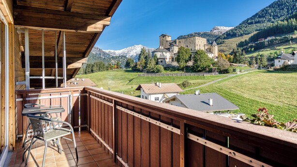 A wooden balcony with a table and chairs, overlooking a castle and mountains. - Hotel Erika (Nauders)