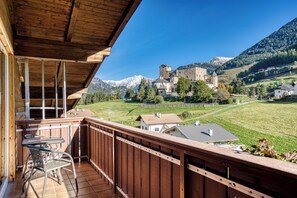 A wooden balcony with a table and chairs, overlooking a castle and mountains. - Hotel Erika (Nauders)