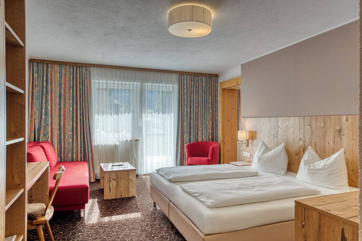 A hotel room with a large bed, a desk, a chair, and a red armchair.
