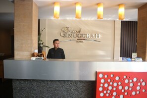Eine Rezeption im Grand Anugerah Hotel mit Kasse, Namensschild und Zahlungsautomaten.