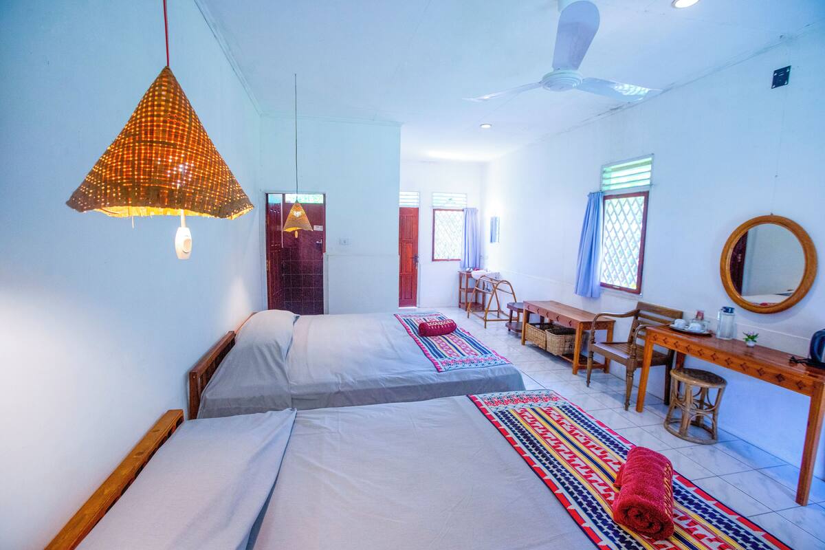 A room with two beds, a desk, a chair, a mirror, and a ceiling fan.