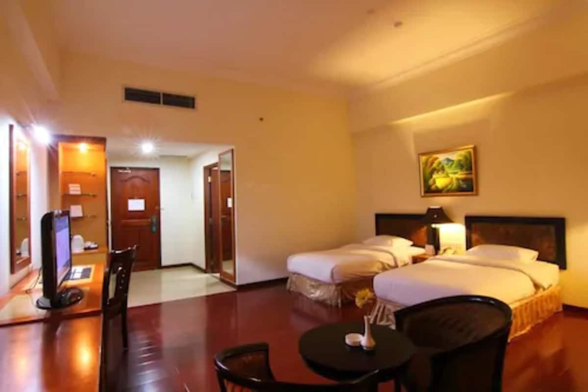 A hotel room with two beds, a desk with a computer, a chair, and a small table.