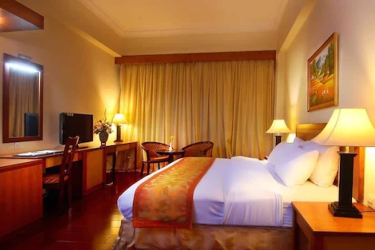A hotel room with a large bed, a desk with a chair, a television, and a painting on the wall.